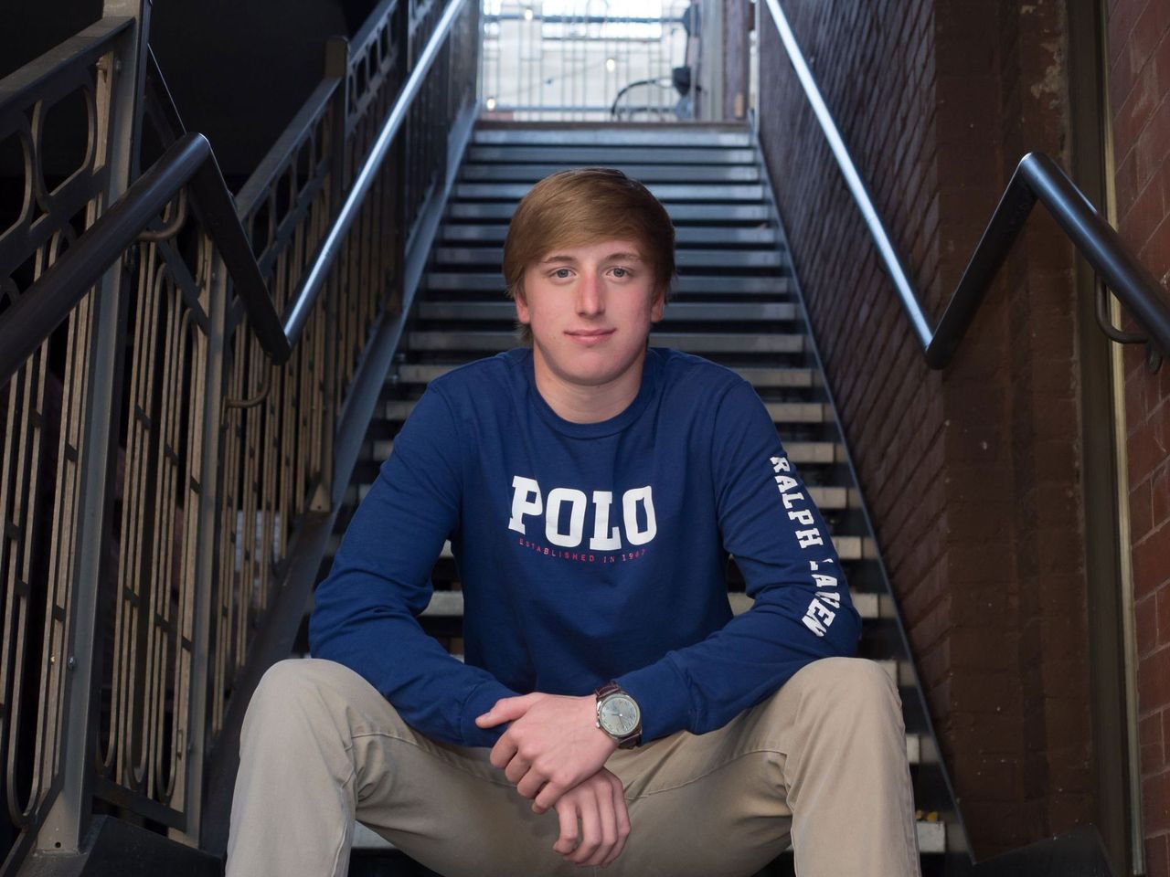 A young man wearing a polo shirt sits on a set of stairs