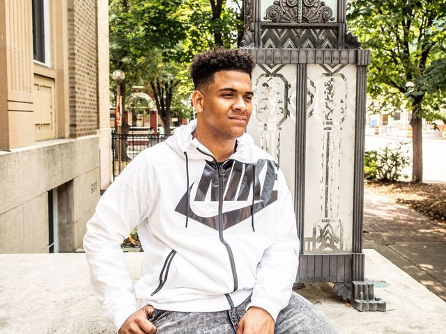 A young man wearing a white nike hoodie is sitting on a sidewalk.