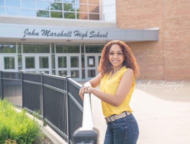 A woman is leaning on a railing in front of a school building.