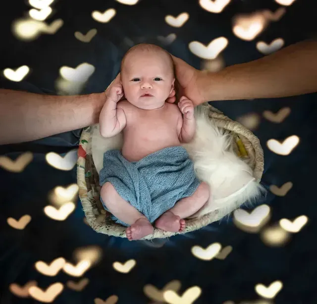 A baby is laying in a basket surrounded by hearts