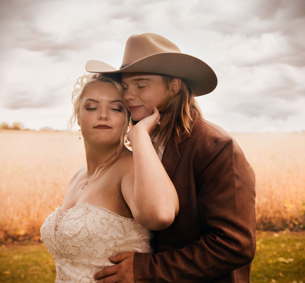 A man in a cowboy hat is hugging a woman in a wedding dress
