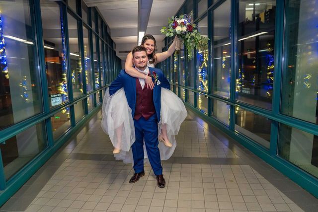 A man is carrying a bride on his shoulders in a hallway.