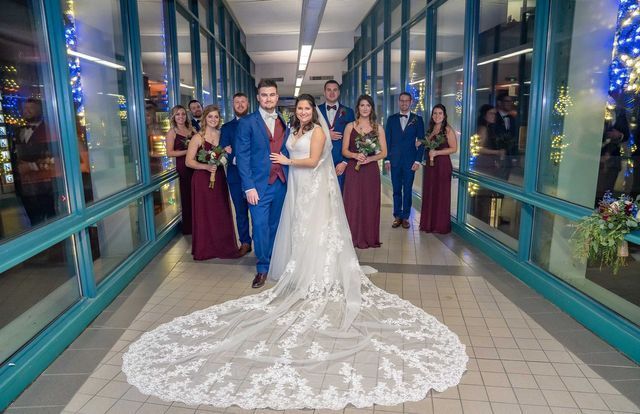 A bride and groom are posing for a picture with their wedding party in a hallway.