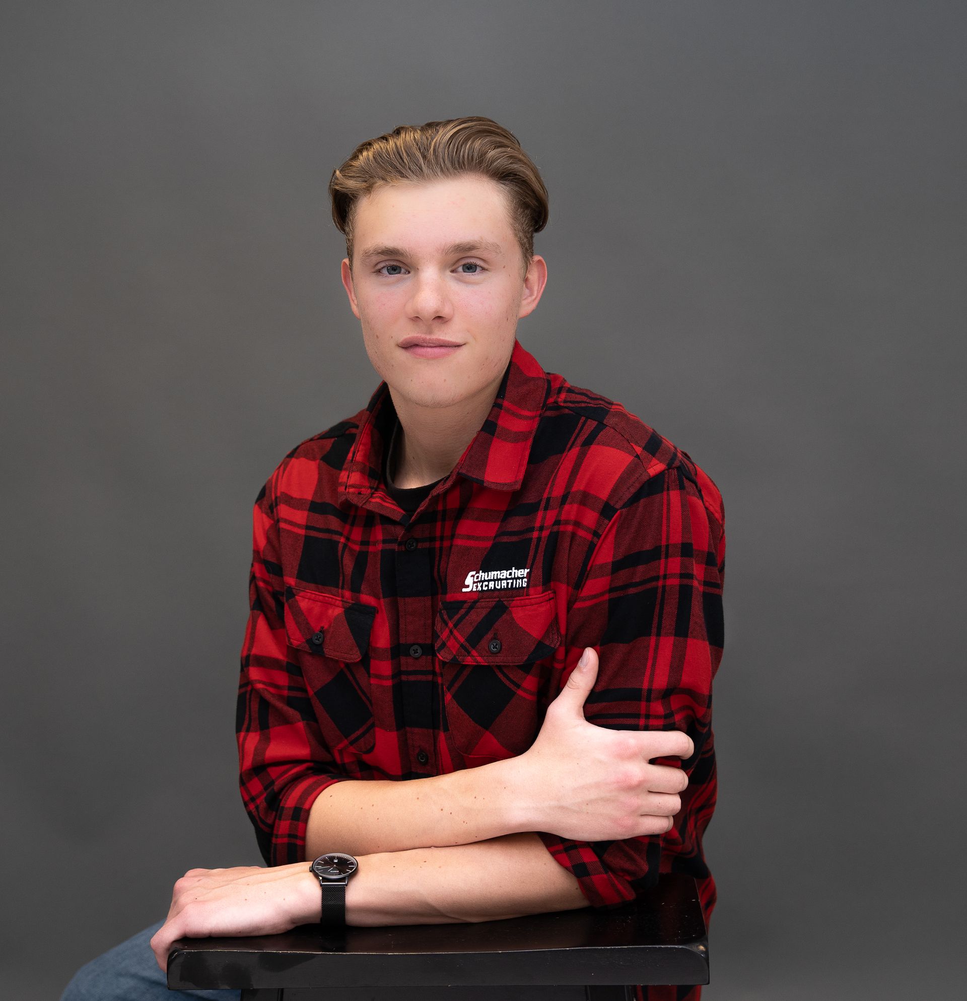 A young man in a red and black plaid shirt is sitting on a table with his arms crossed.