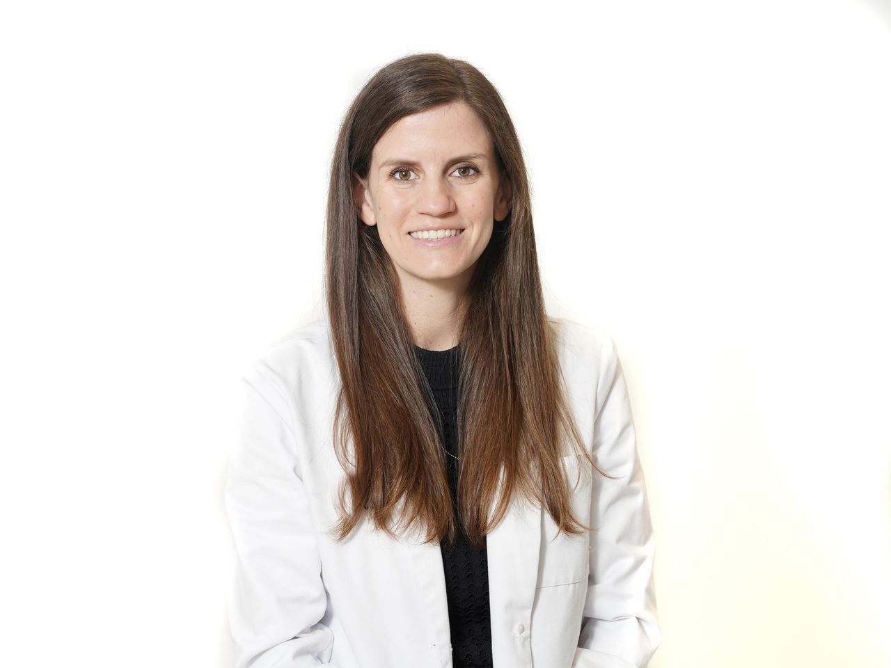 A woman in a white lab coat is smiling for the camera.