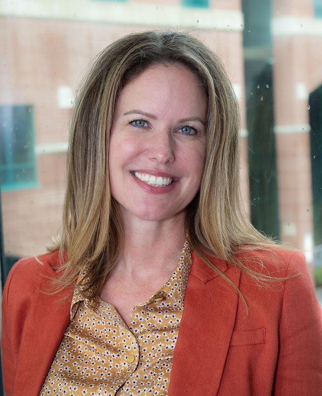 A woman wearing an orange jacket and a yellow shirt is smiling for the camera.