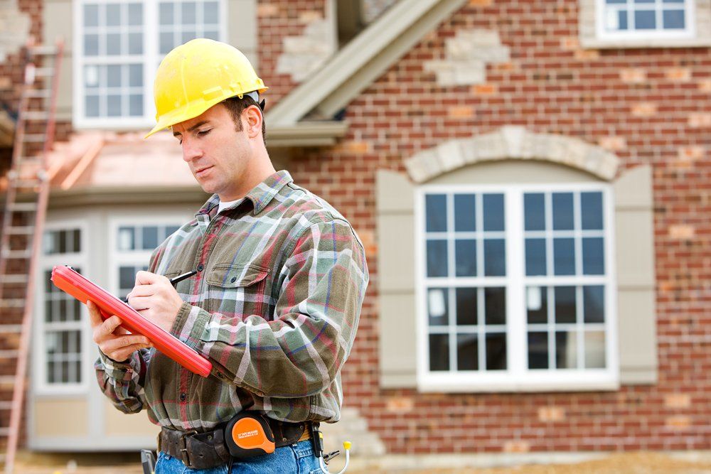A construction worker is writing on a clipboard in front of a brick house.