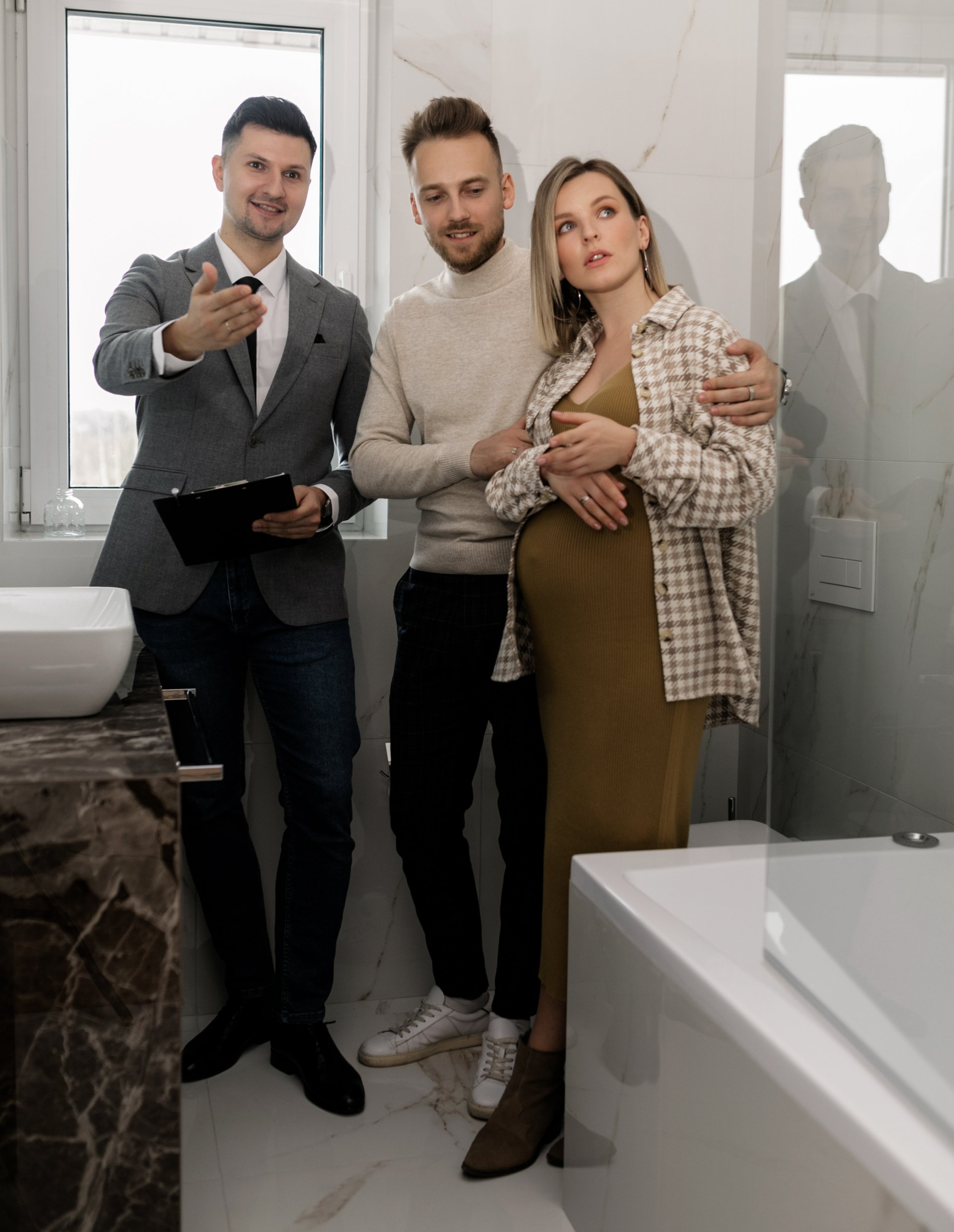 A pregnant woman is standing next to two men in a bathroom.