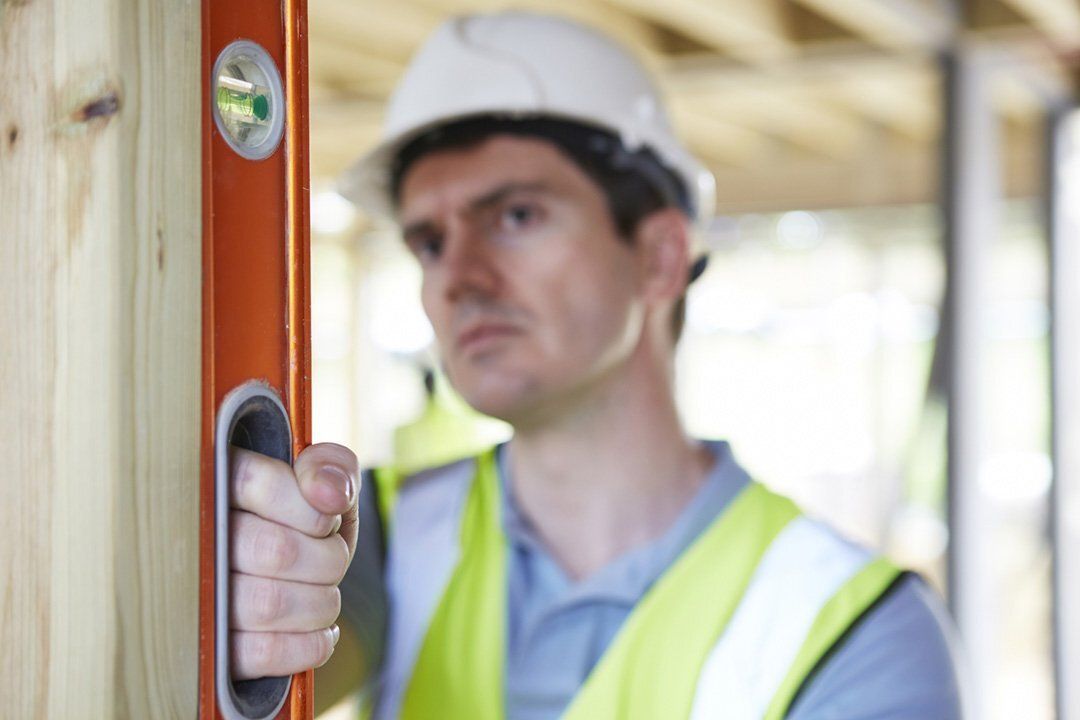 A man wearing a hard hat and safety vest is holding a level