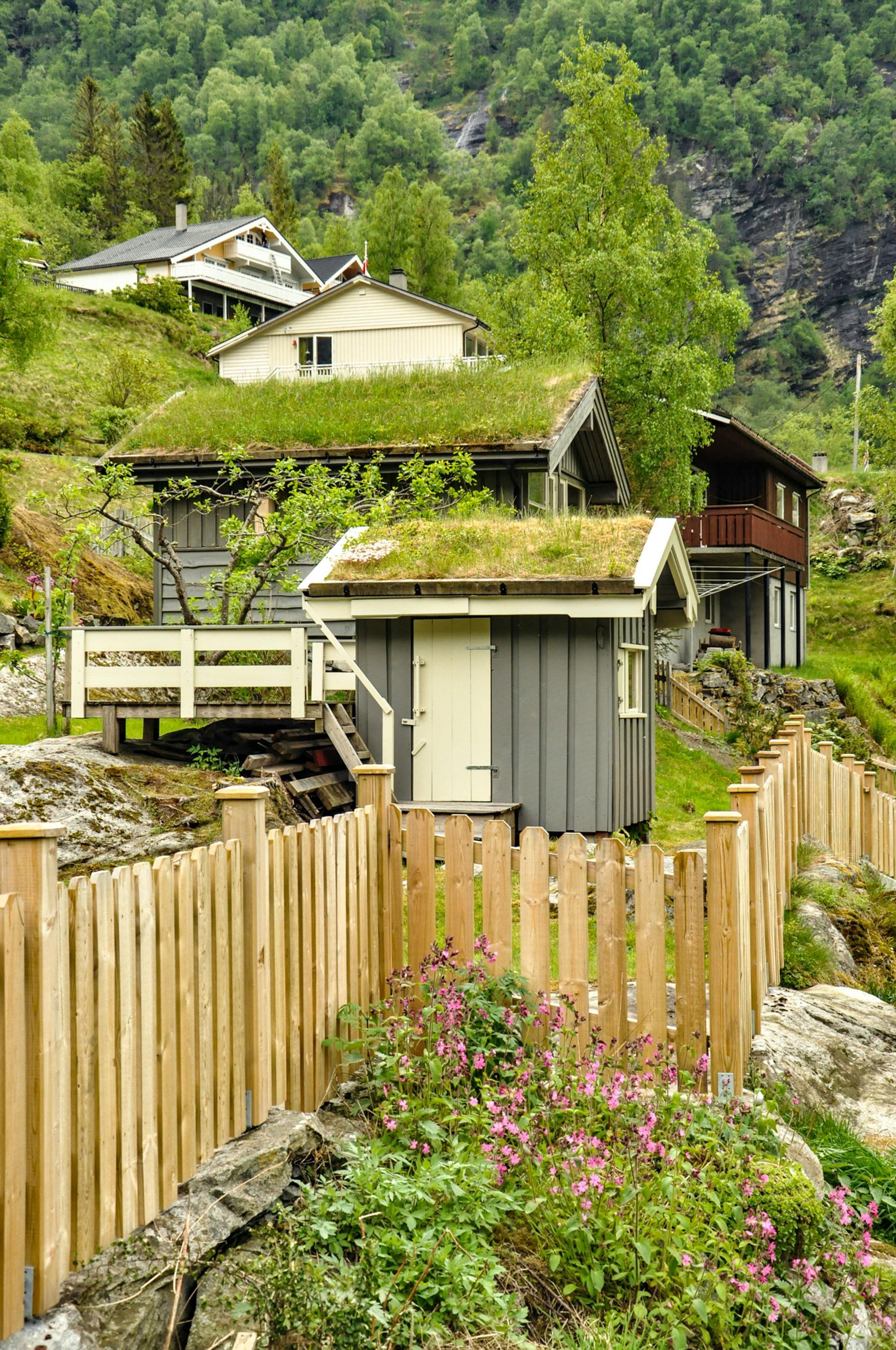 A wooden fence surrounds a small house with a green roof.