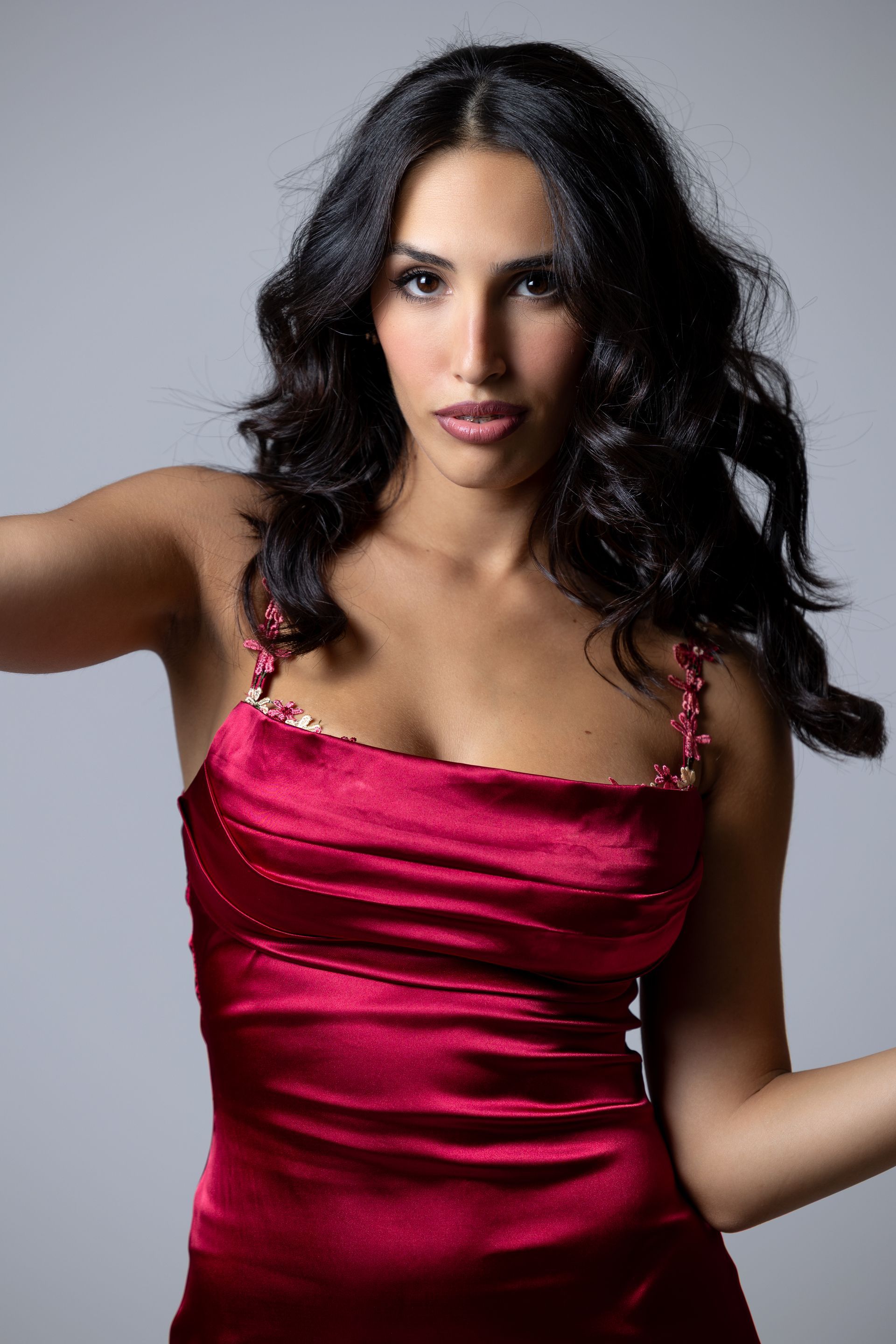 Donna sorridente con lunghi capelli scuri e ondulati, in abito di raso rosso.