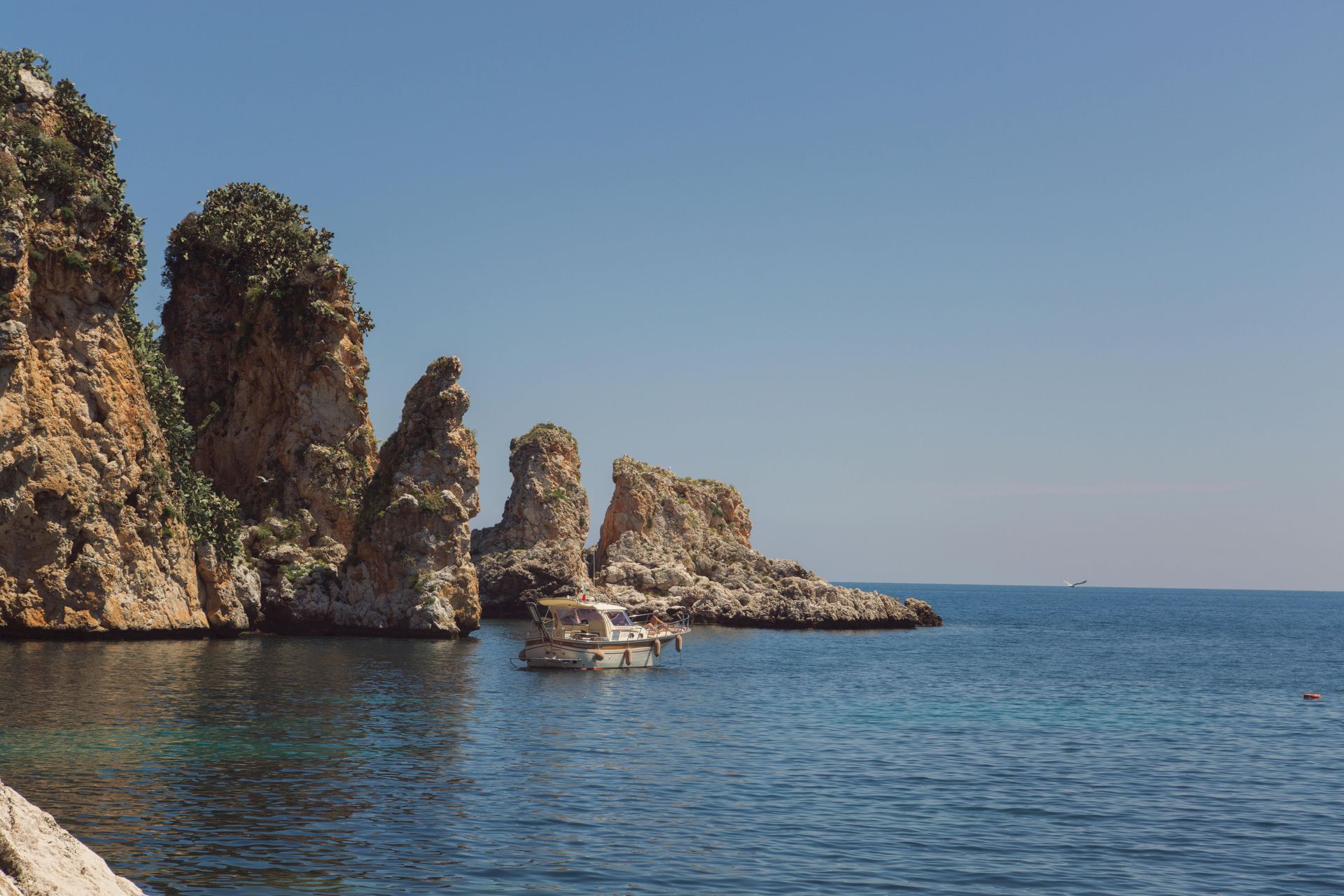 Costa rocciosa con una barca sull'acqua blu sotto un cielo limpido.