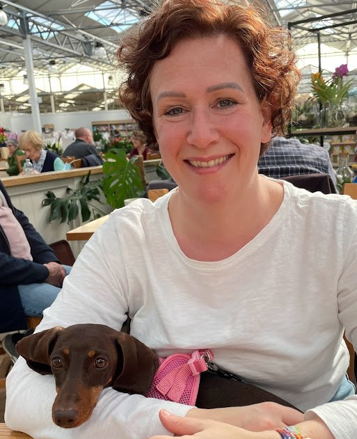 A woman is sitting at a table with a small brown dog on her lap