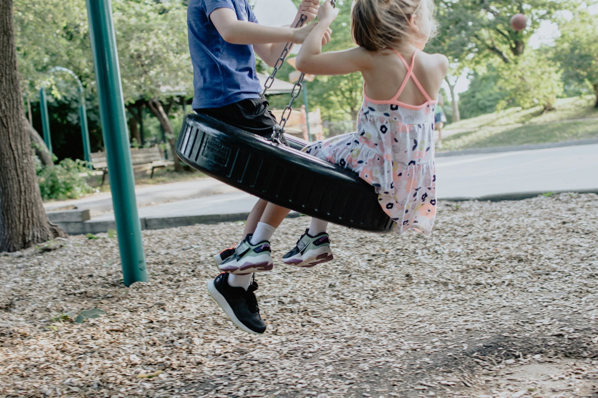 A boy and a girl are swinging on a tire swing in a park.