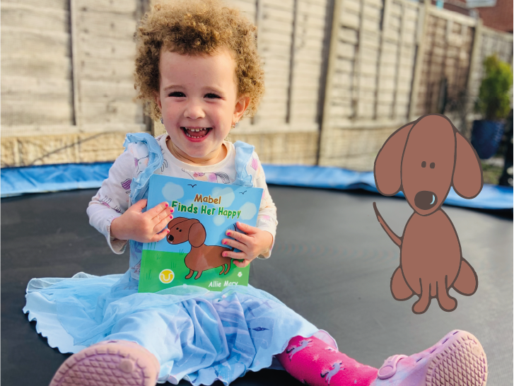 A little girl is sitting on a trampoline holding a book about a dog.