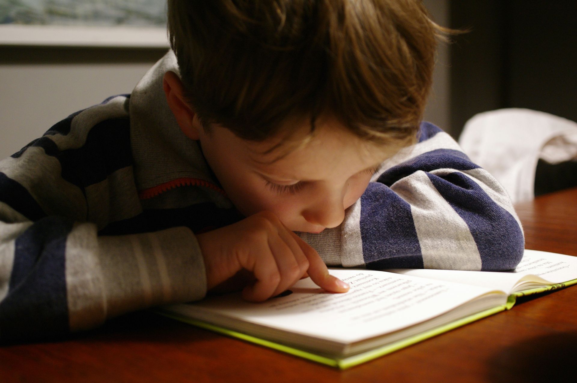 A young boy is laying on his stomach reading a book.