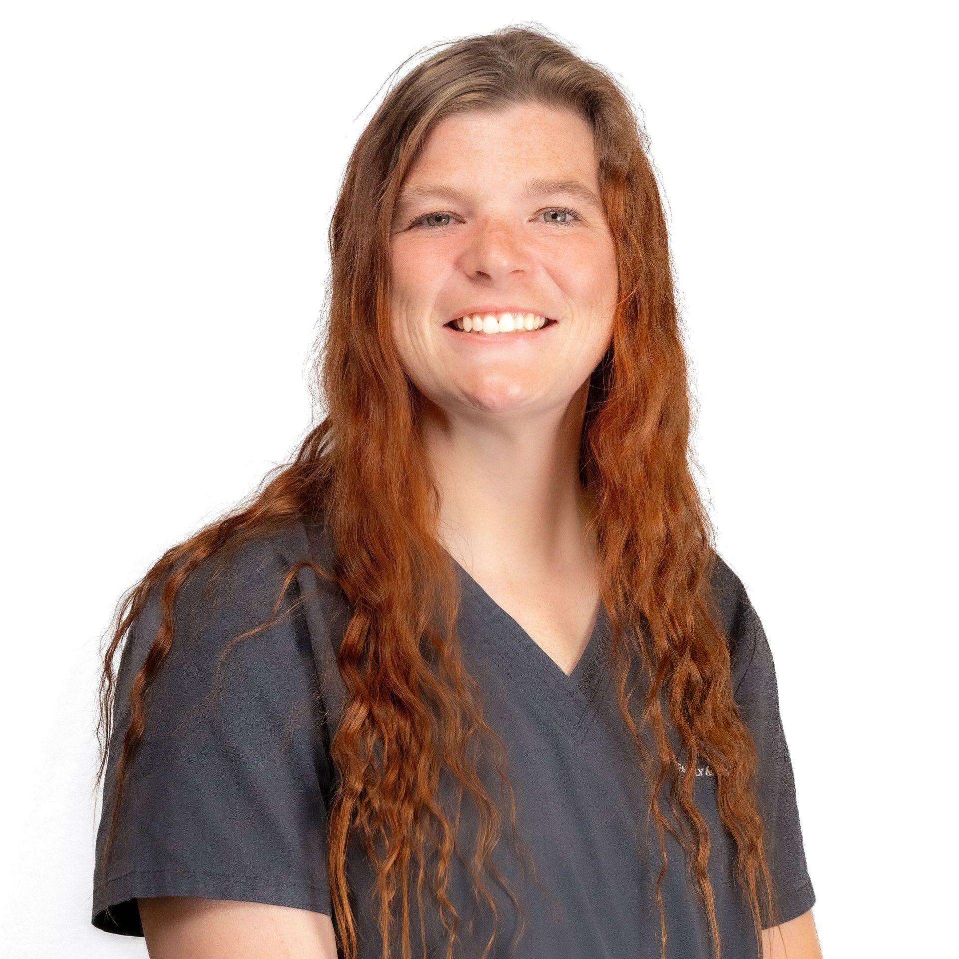 a woman with long red hair is wearing a gray scrub top and smiling .