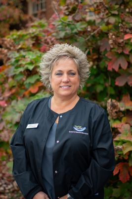 A woman in a black jacket is standing in front of a bush.