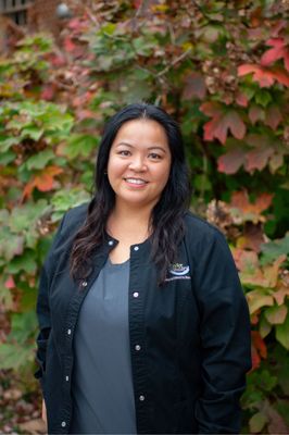 A woman in a black jacket is standing in front of a bush.