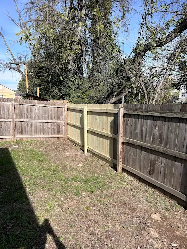 Wooden fence in a yard; the new section of fence is a lighter color than the older sections.