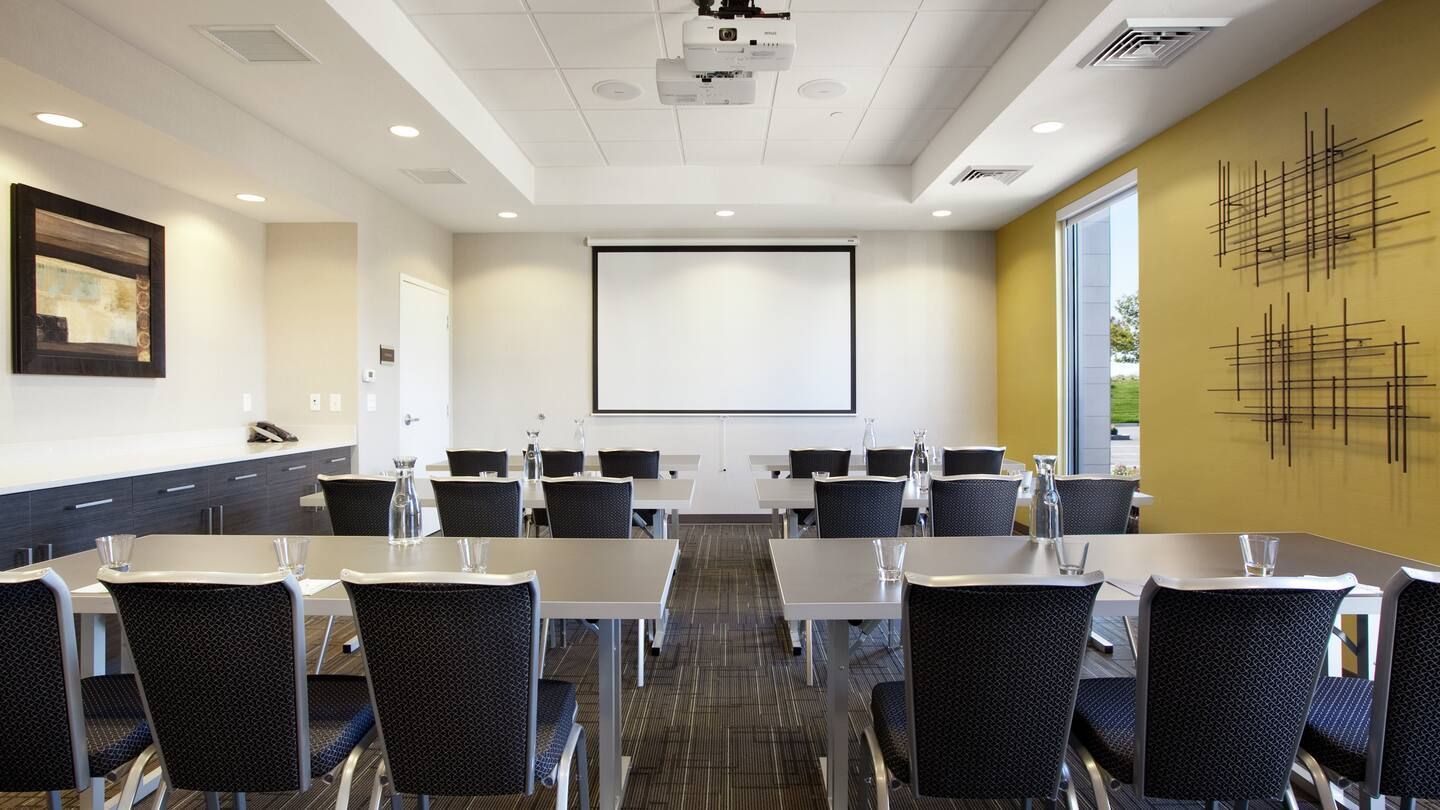 A conference room with tables and chairs and a projector screen