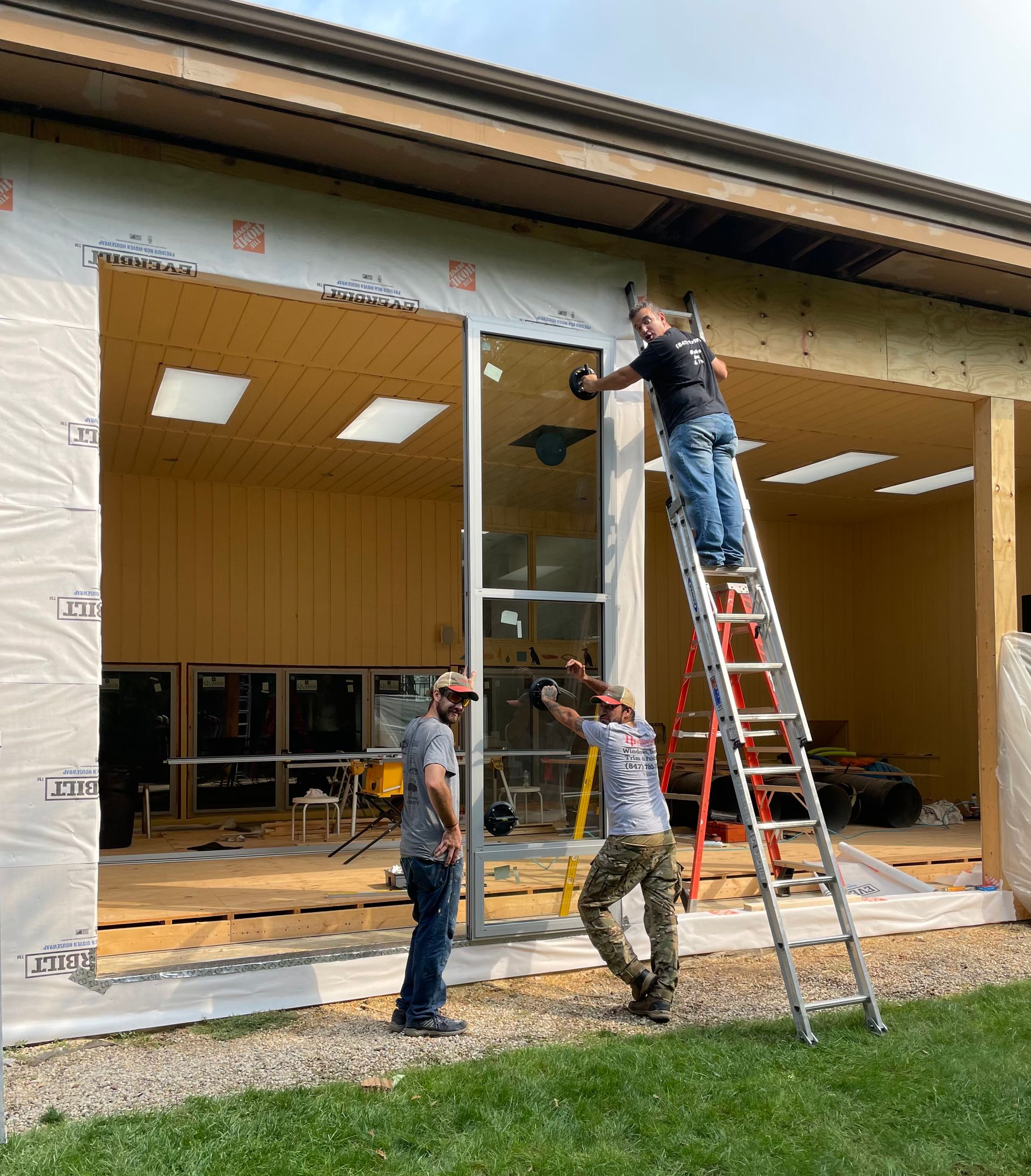 Three people installing a window in a building under construction, using a ladder.