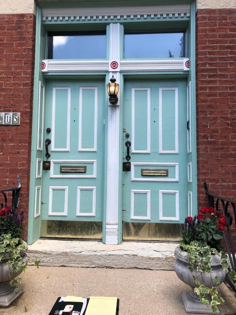 Two turquoise doors with white trim and a shared window above, set in a red brick building.