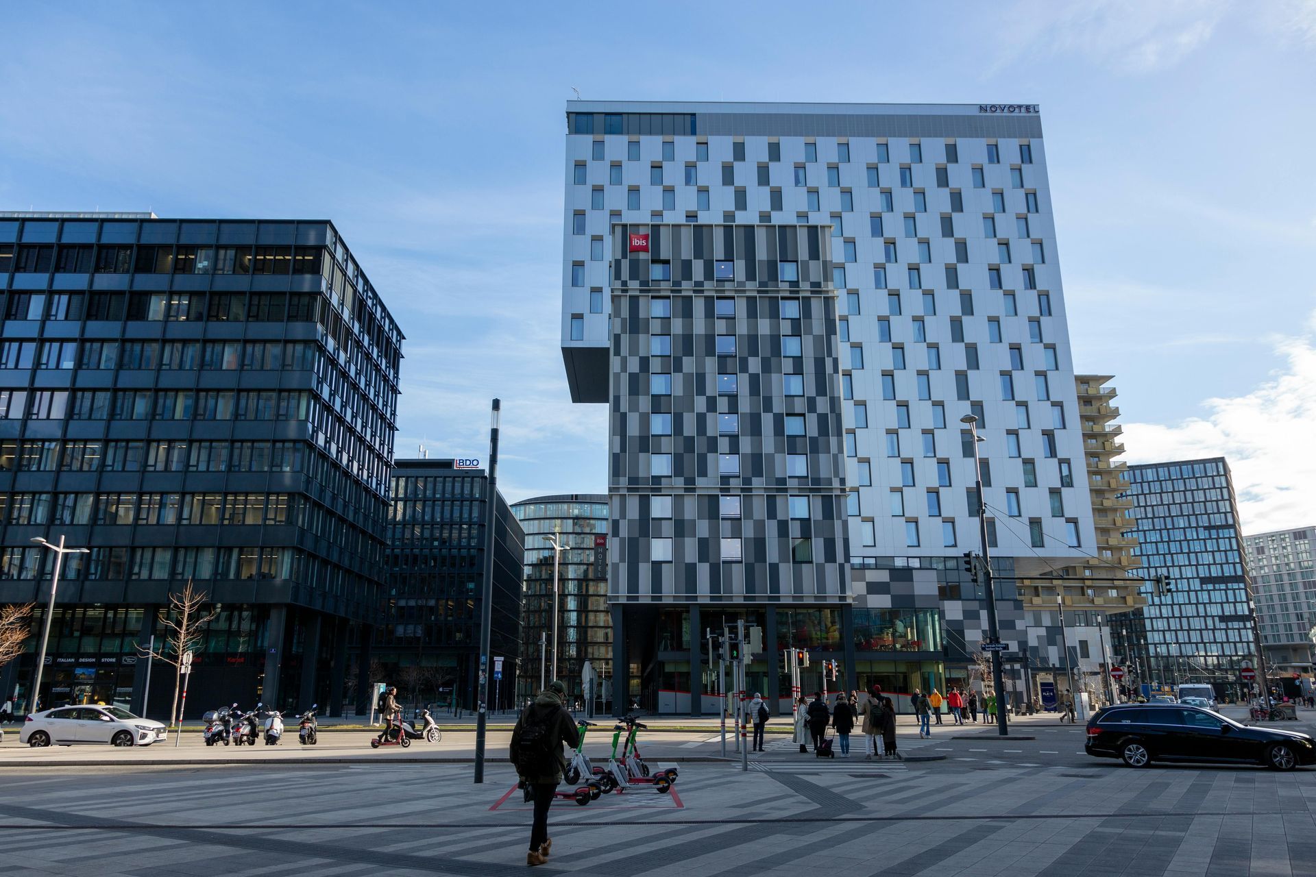 A professional in a suit reviews blueprints on a table with two individuals in a modern, well-lit interior.
