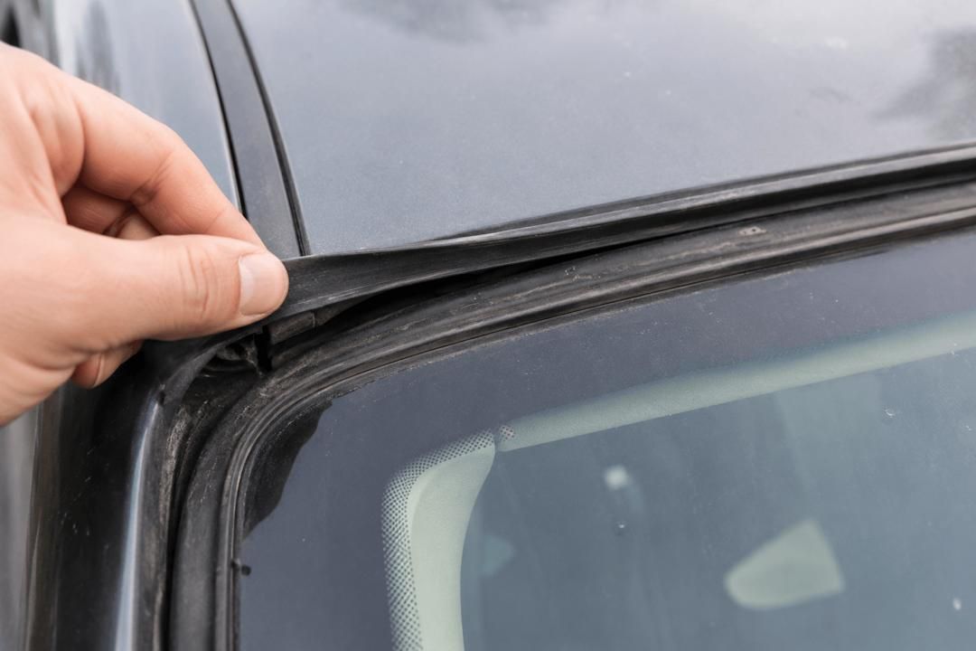 Hand lifting a rubber weatherstripping seal along the edge of a car window