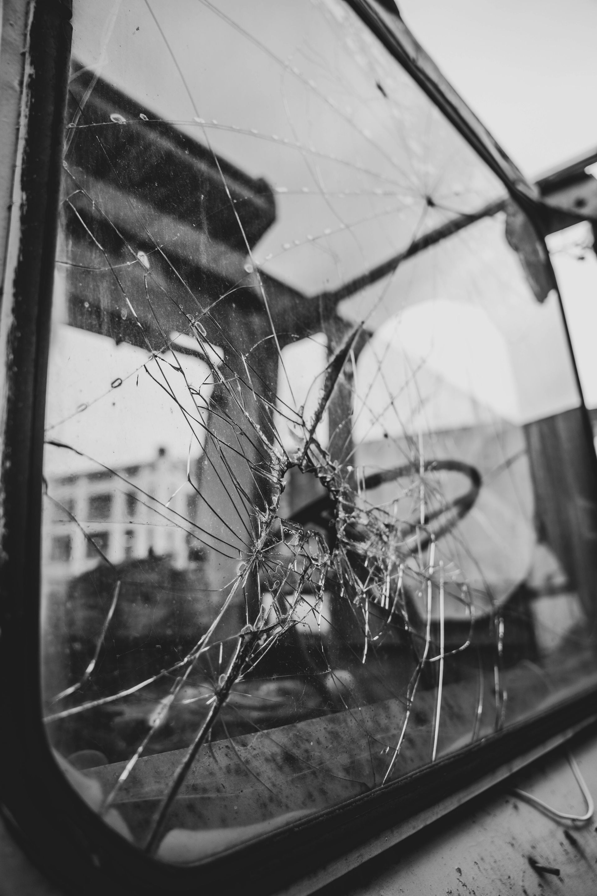Cracked windshield of an old vehicle. Steering wheel visible inside. Black and white.