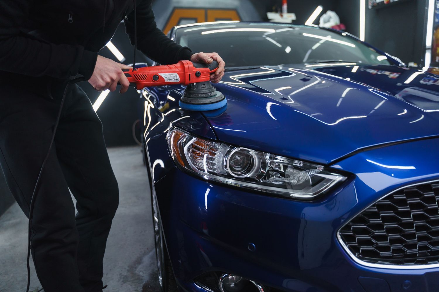 A man is polishing a blue car with a machine.