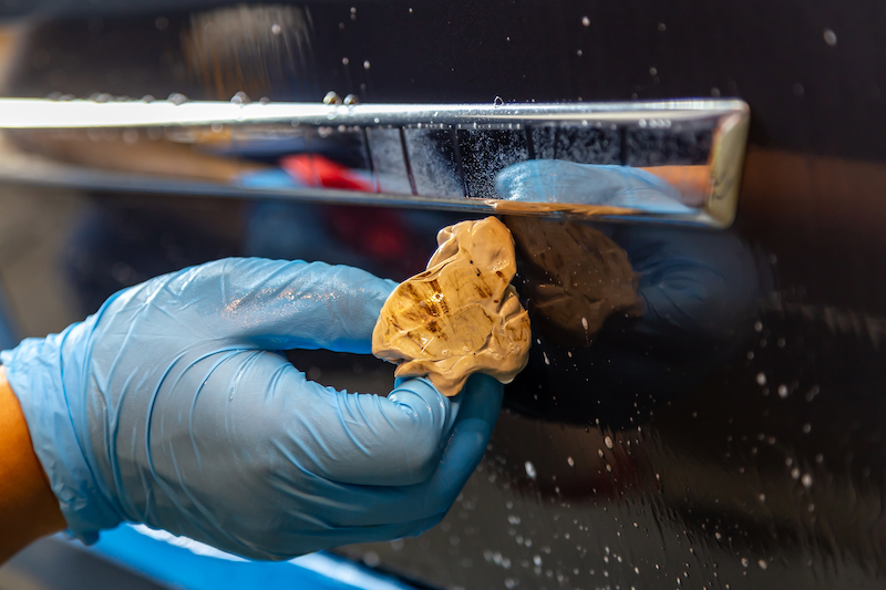 A person wearing blue gloves is cleaning a car door with a cloth.