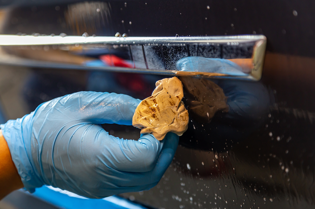 A person wearing blue gloves is cleaning a car door with a cloth.