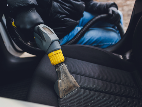 A person is cleaning the seats of a car with a vacuum cleaner.