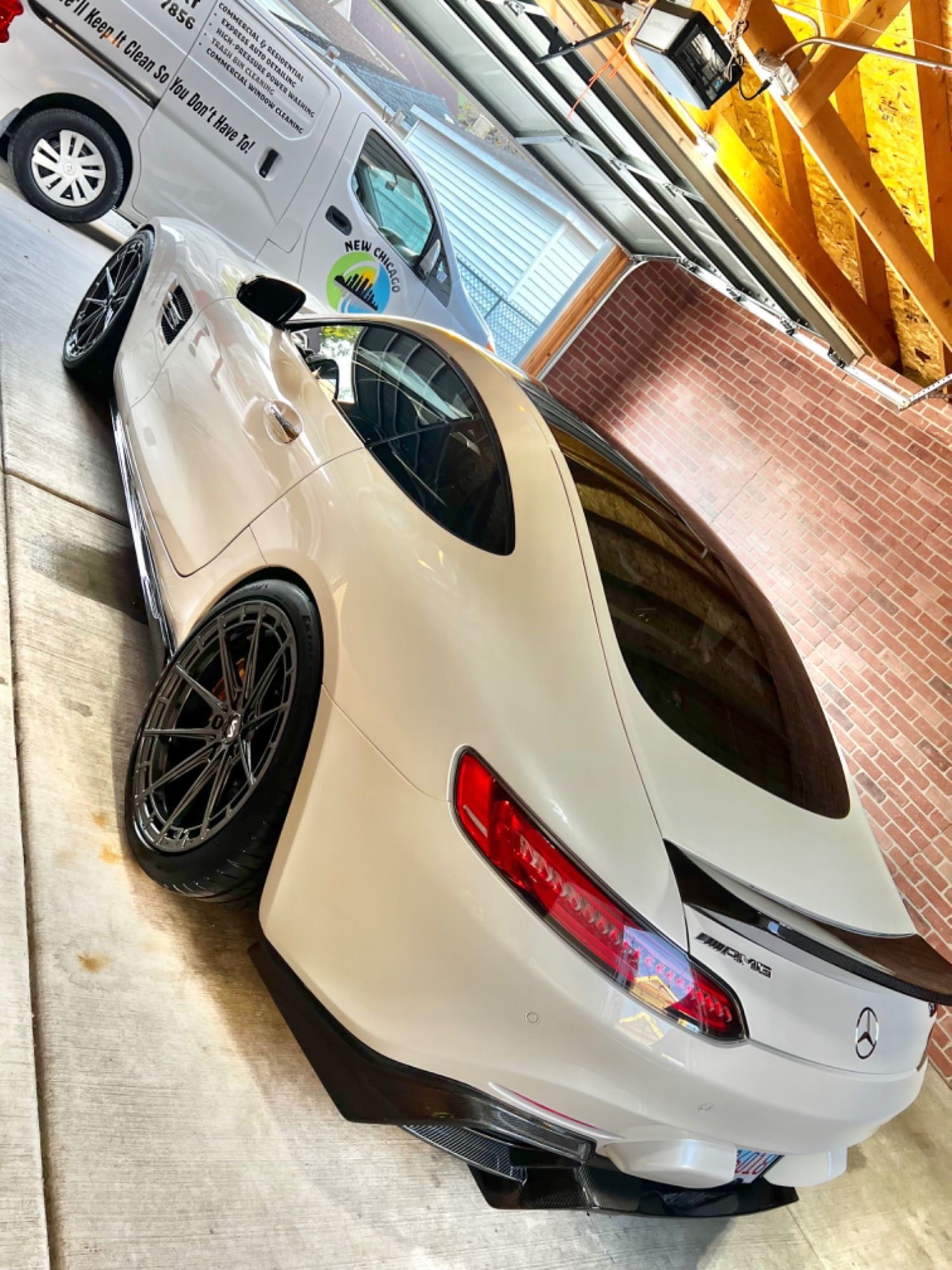 A white sports car is parked in a driveway next to a white van.
