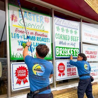 Two men are cleaning a restaurant window with a vacuum cleaner.