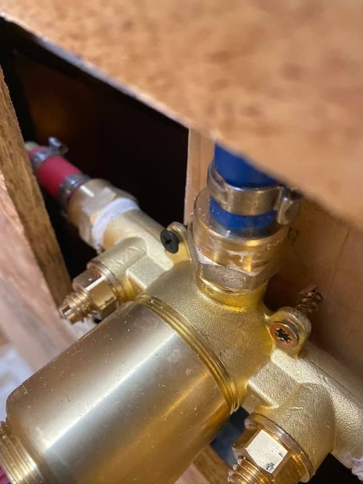 Close-up of brass plumbing valve with blue and red pipes inside a wooden cabinet