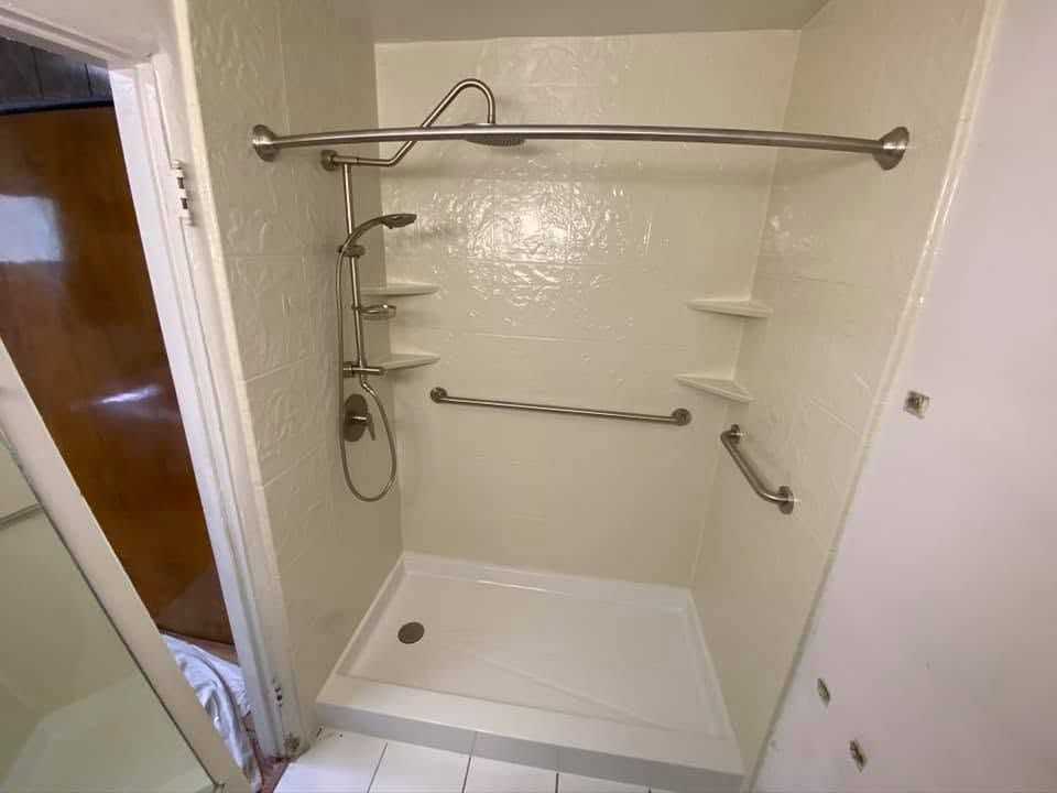 Accessible shower with grab bars, fold-down seat, handheld shower, and tiled walls