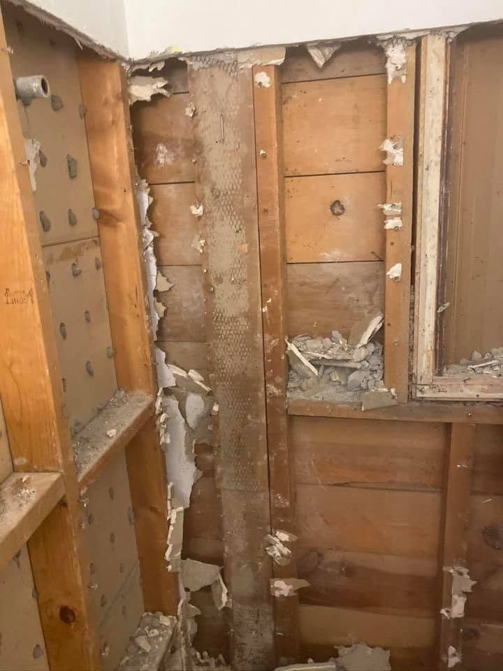 Exposed wooden wall framing with insulation removed and plaster debris in a damaged interior space