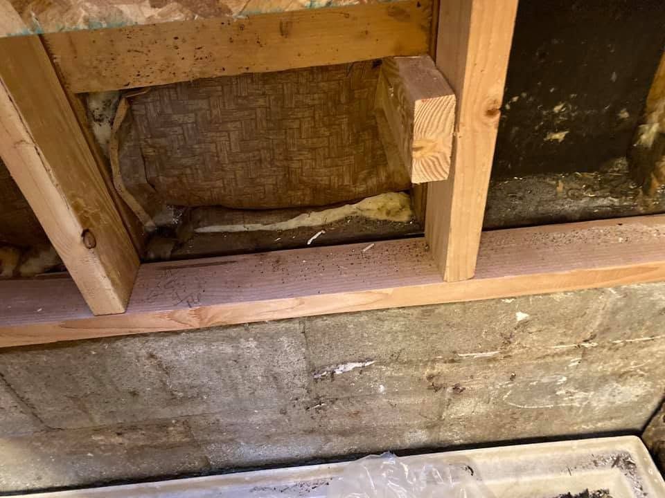 Exposed wooden wall framing with insulation and weathered siding, showing a damaged lower section