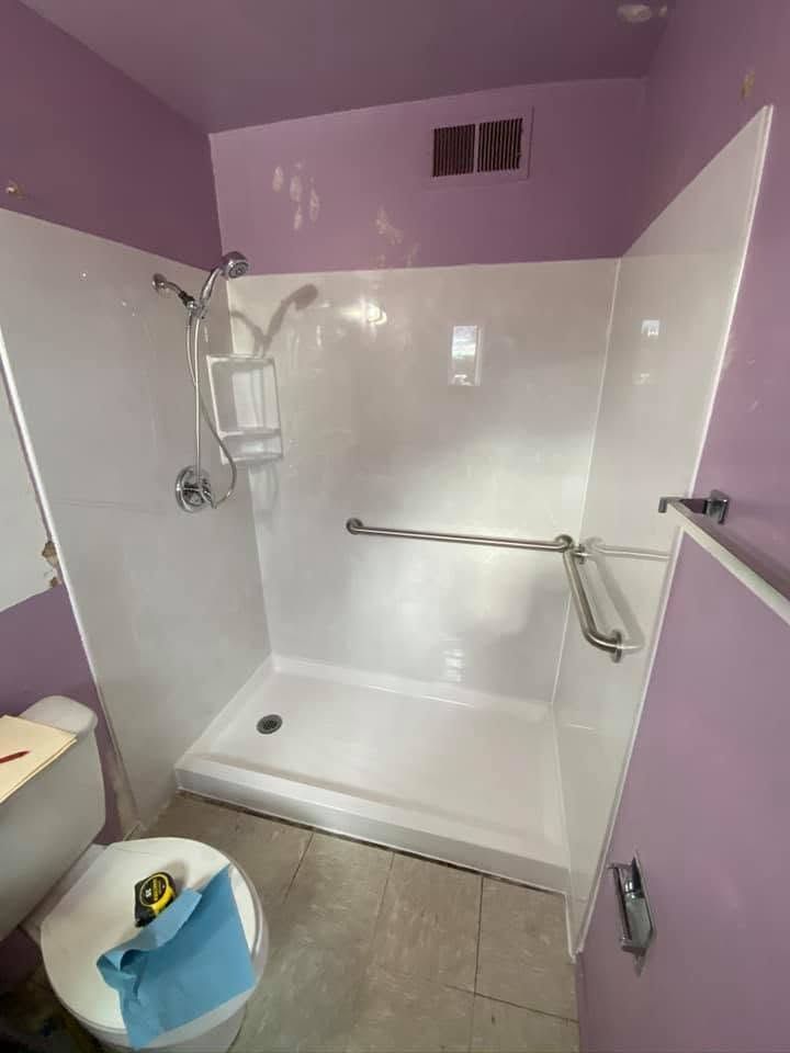 Accessible shower stall with grab bars, white walls, and a fold-down seat in a small bathroom