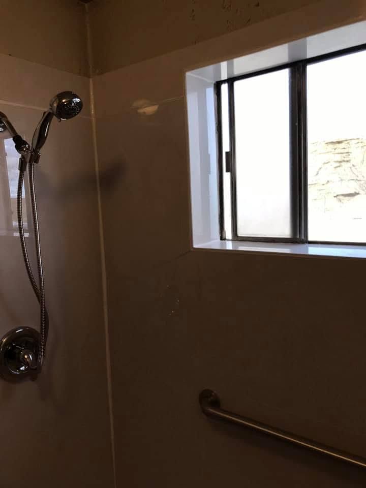 Shower stall with chrome fixtures, grab bar, and a small window letting in daylight.