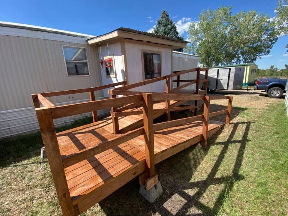 Wooden wheelchair ramp with railings leading to a beige mobile home in a grassy yard