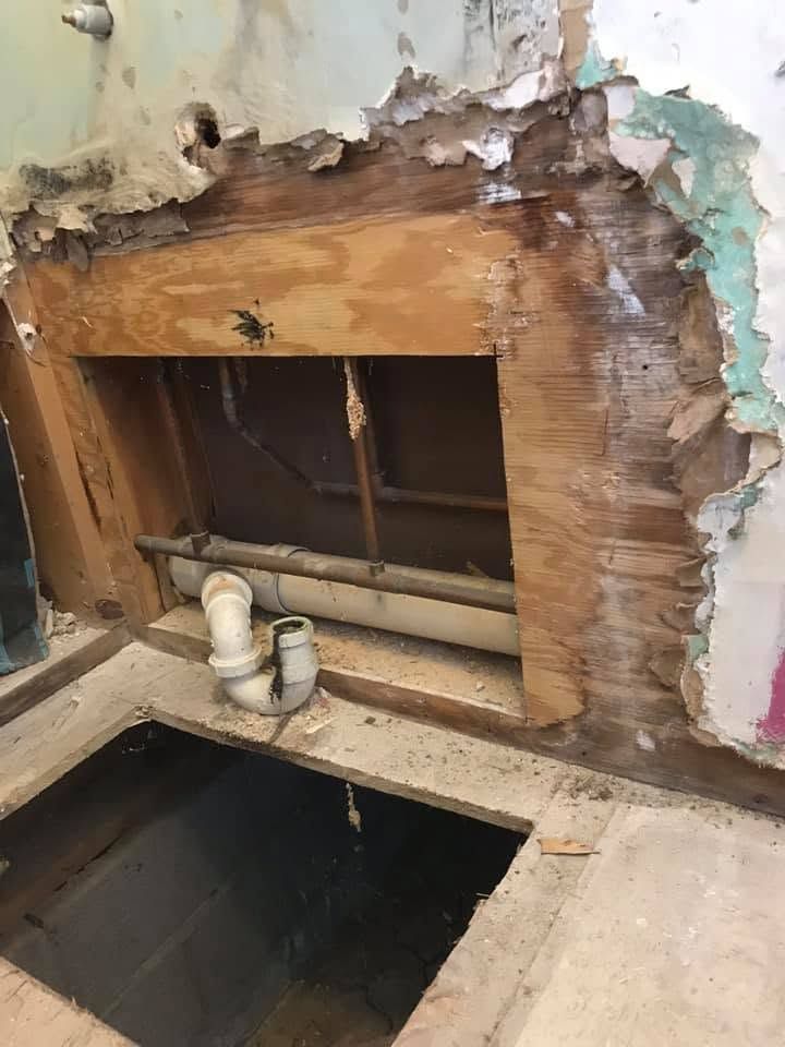 Damaged bathroom wall with exposed plumbing and a large open hole in the floor