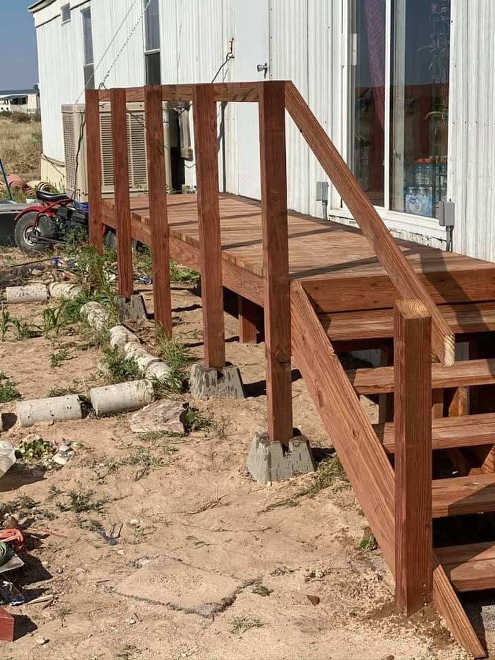 Wooden accessibility ramp with railings beside a building entrance on a dirt lot.