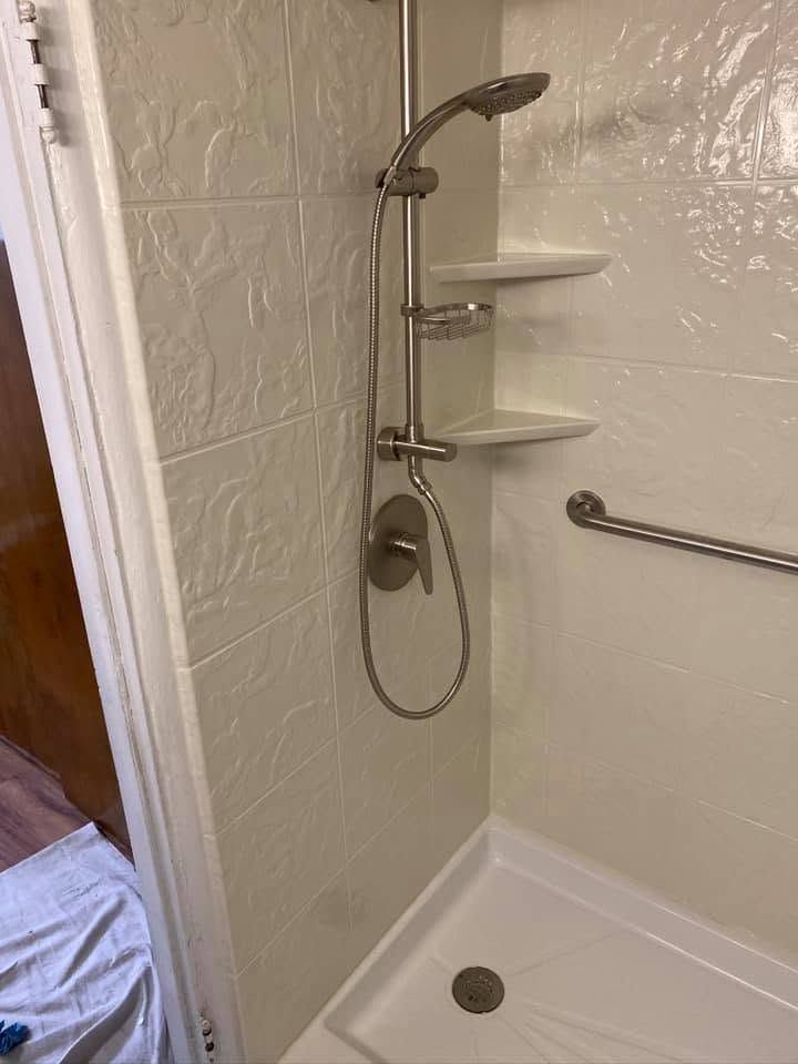 Accessible shower stall with grab bar, corner shelves, handheld showerhead, and tiled walls