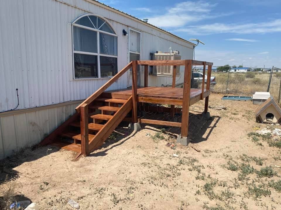 Wooden accessibility ramp and stairs beside a white building in a sandy yard