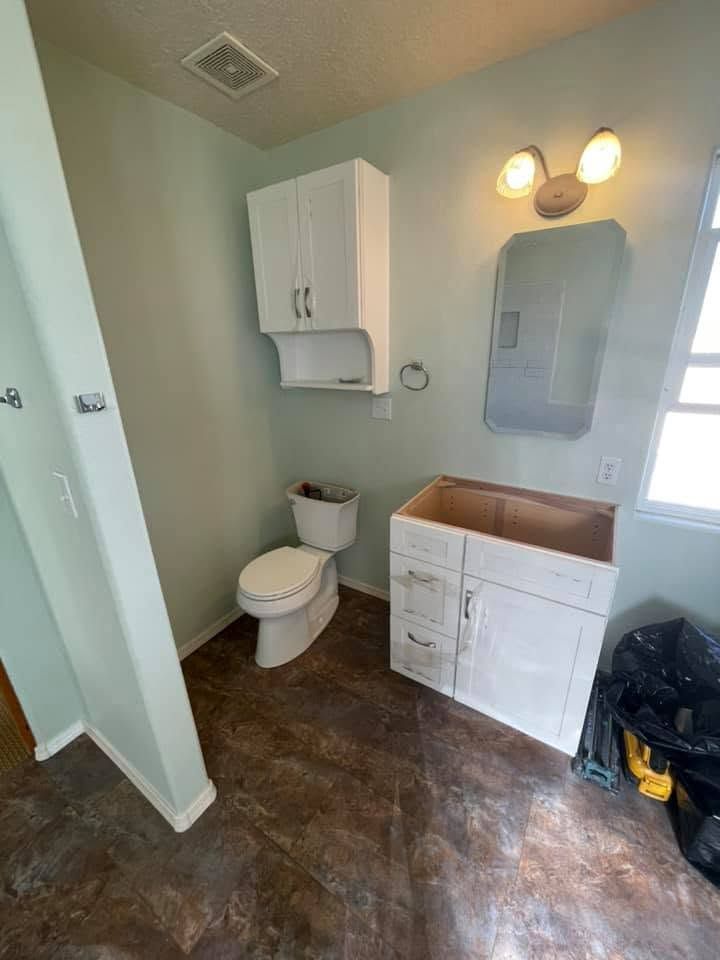 Small bathroom with toilet, white vanity, wall mirror, and pale green walls.