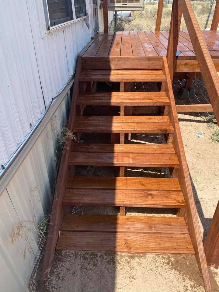 Wooden outdoor stairs beside a white building, leading to a deck.