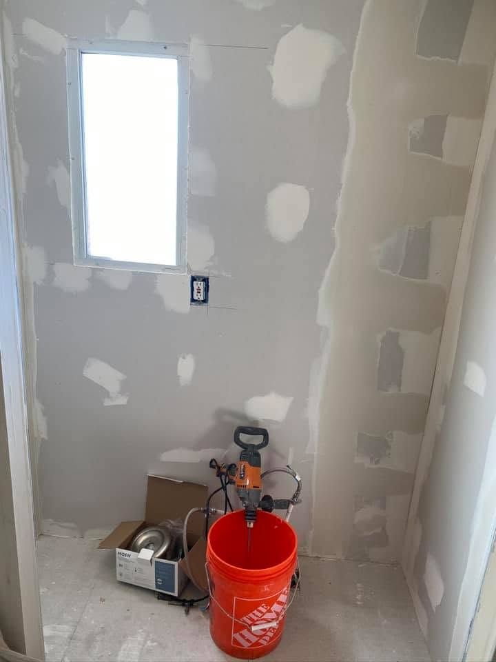 Small unfinished shower with drywall patches, window, outlet, and red bucket on the floor